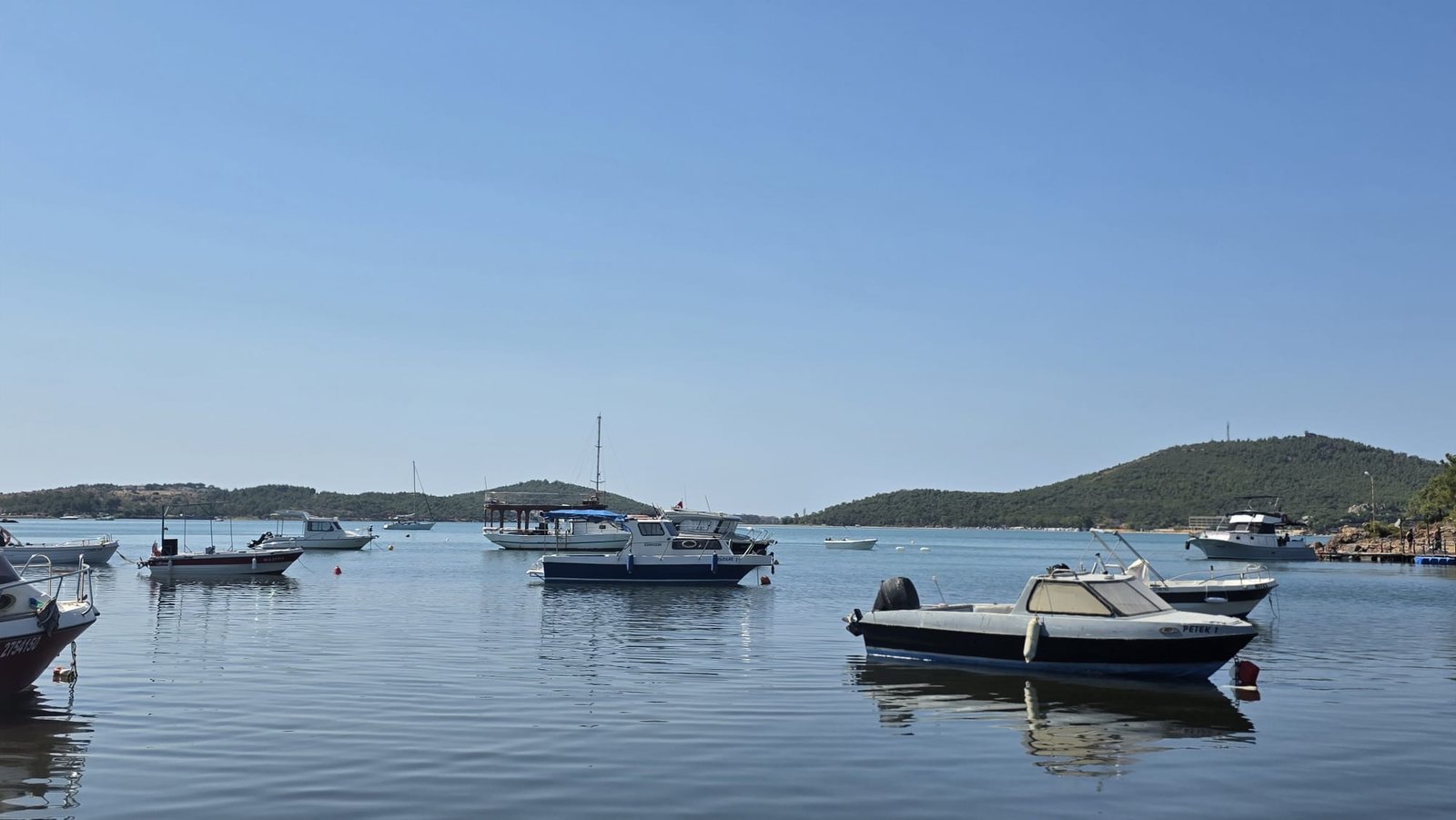 Paddleboarding in Ayvalık: The Shipwreck Route to Delikli Taş Calm anchorage at Paşa Limanı, Ayvalık, with small fishing boats moored on mirror-flat water and green hills in the background