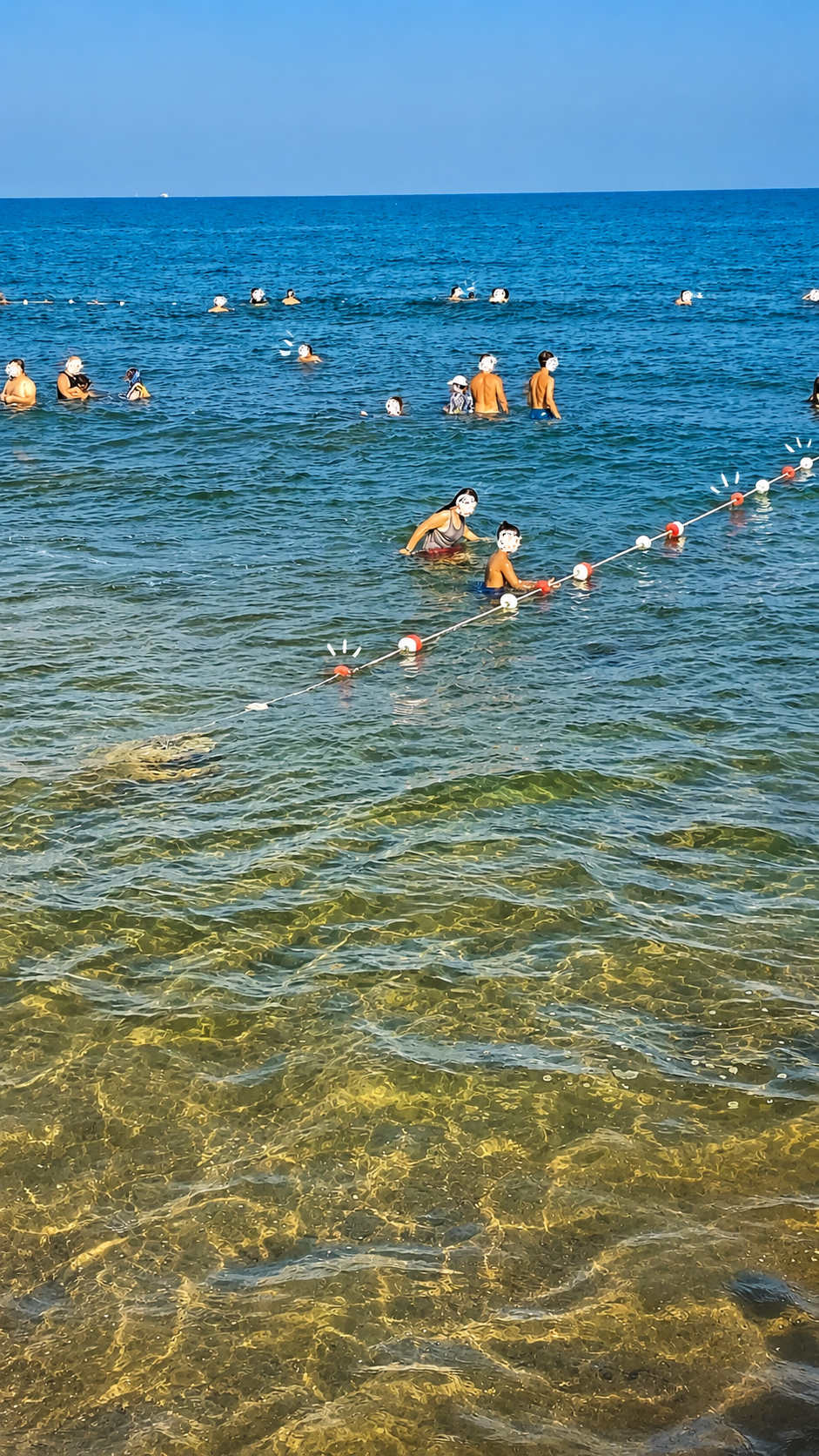 Paddleboarding at Soli Pompeiopolis Swimmers and a marked swim-zone buoy line in clear-to-hazy Mediterranean water at Mezitli beach