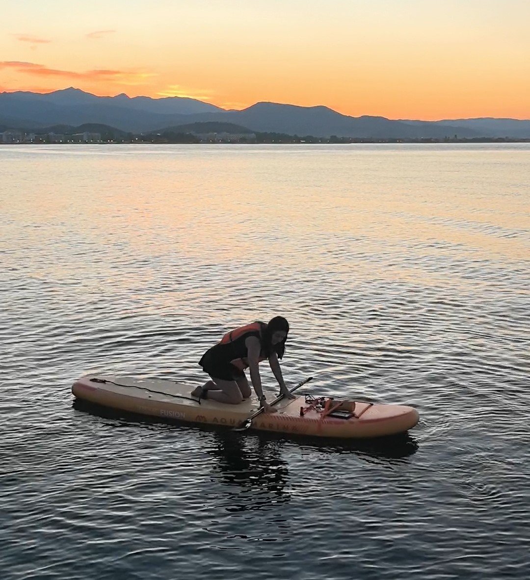 How to Stand Up Paddle Board: Complete Beginner's Guide (2026) Beginner kneeling centered on an inflatable paddle board on calm water
