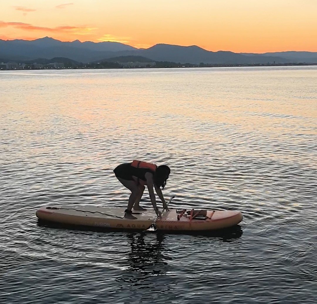 How to Stand Up Paddle Board: Complete Beginner's Guide (2026) Paddler in a low crouch moving one foot at a time from kneeling to standing on a SUP
