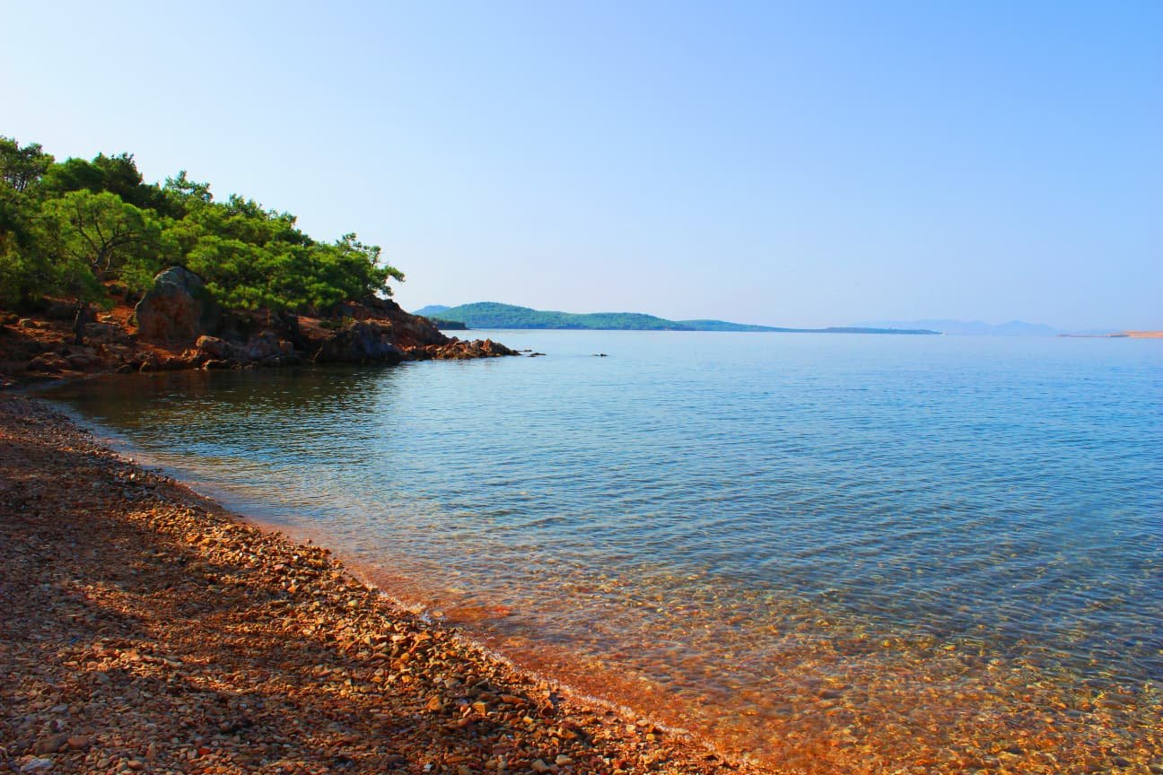 Clear turquoise water and pebble entrance at Ortunç Beach, Cunda Island, with visible seabed