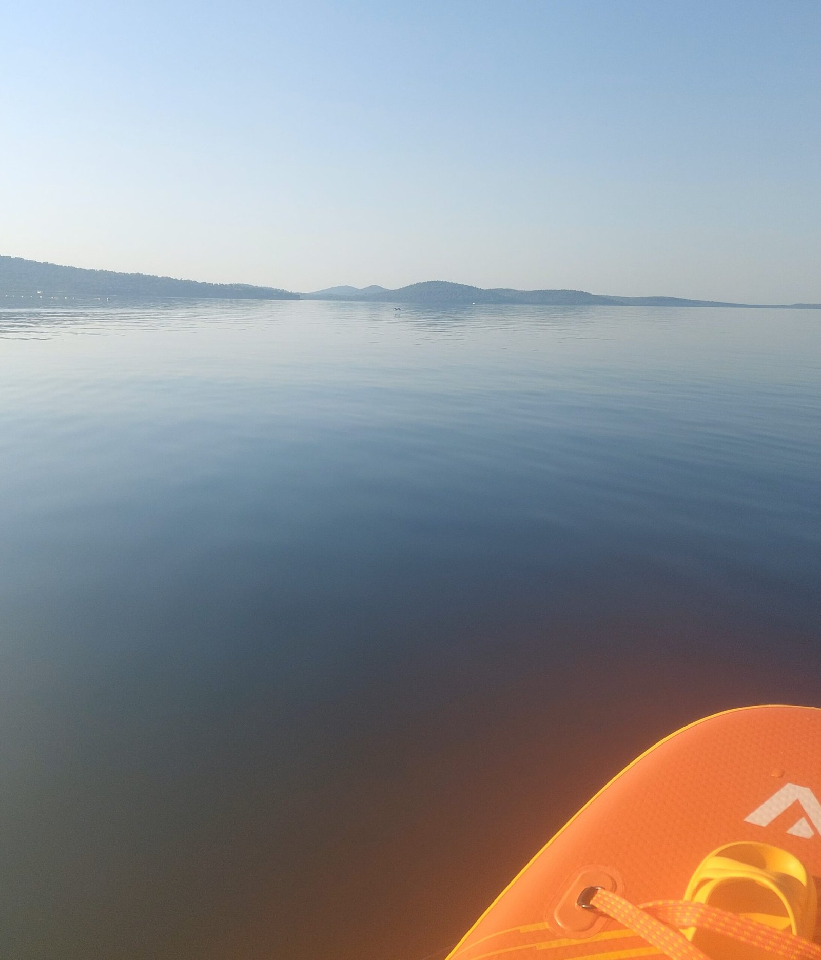 View from the nose of an inflatable paddleboard on flat, glassy water at Ortunç Bay, Cunda Island, at sunrise