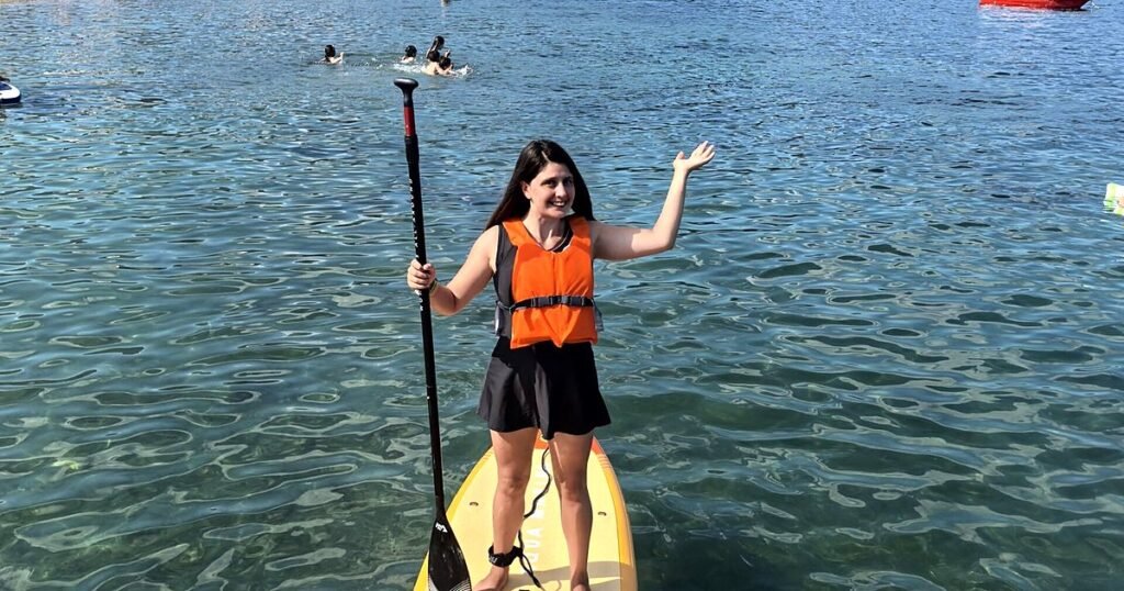Deniz on a paddleboard wearing an orange buoyancy aid and leash