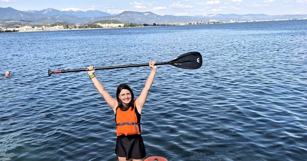 Deniz holding a SUP paddle overhead while standing on her board