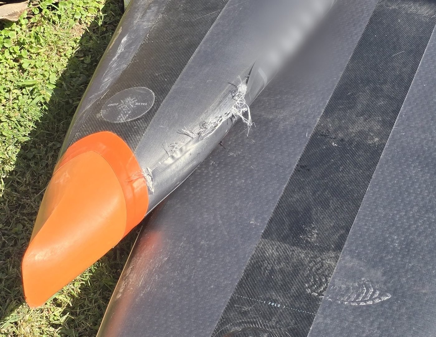 How to Store a Paddleboard: Inflated or Deflated? A burst inflatable paddleboard lying on grass, the skin split open with drop-stitch threads hanging out of the tear